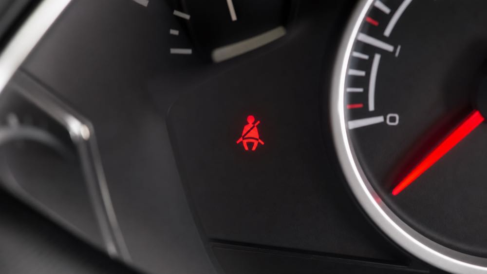 Red seat belt warning light illuminated on a modern car dashboard