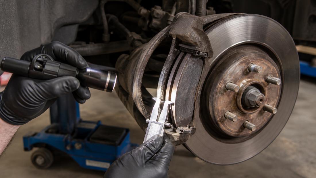 Worn brake pad and rotor being inspected during brake service